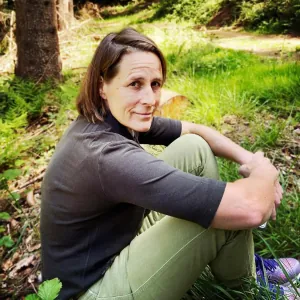 Susanne Hartmann sitzt entspannt auf dem Waldboden