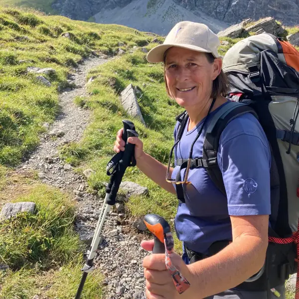 Susanne Hartmann mit Rucksack und Wanderstöcken auf einem Bergpfad, Daumen nach oben